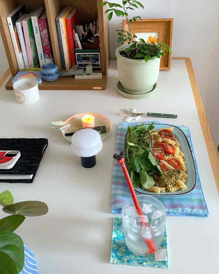 White table and natural wooden bookshelf in a small room, home cafe space with pasta on tablecloth and indoor plant