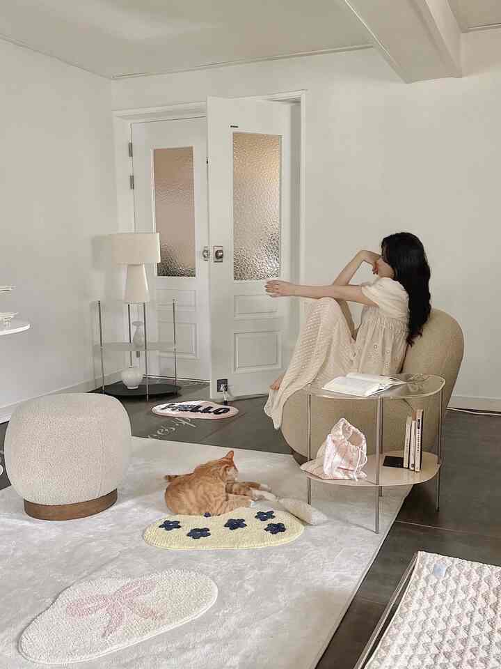 White and beige toned living room featuring a cat lying on the rug with an armchair and glass metal side table creating a cozy atmosphere