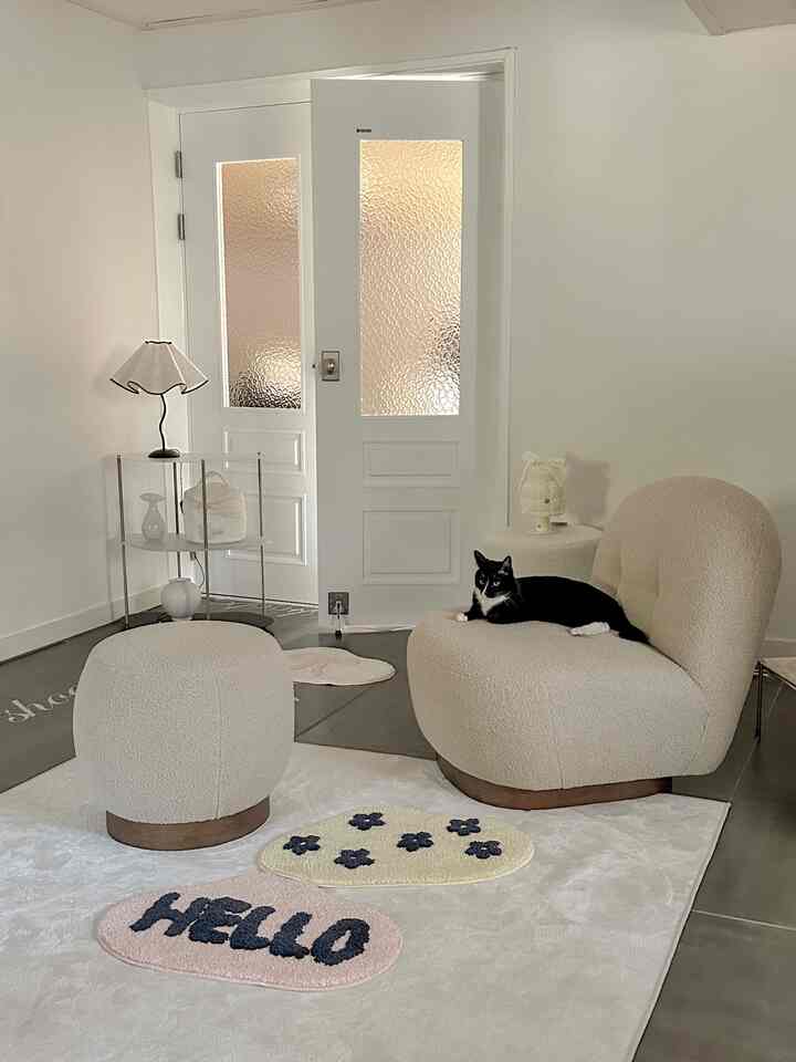 Beige-toned living room featuring plush armchair and ottoman with a black cat resting, creating a cozy atmosphere