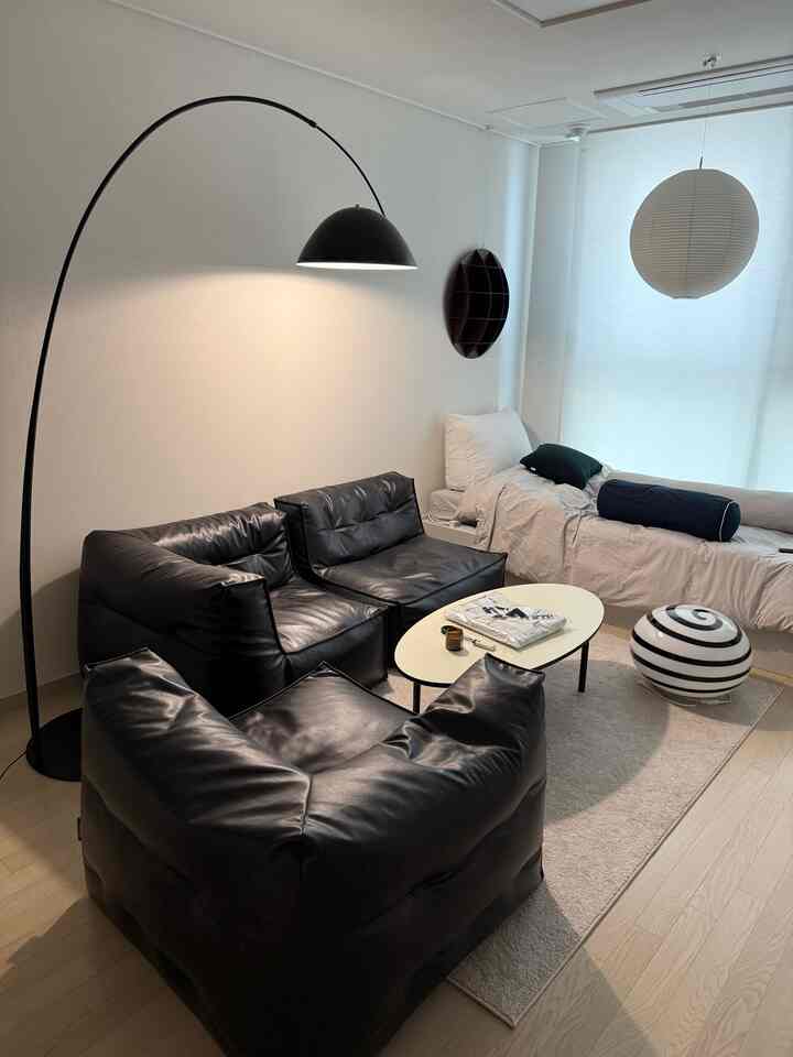 黒い光沢のあるレザービーンバッグソファとソファ、ライトグレーのラグ、アーチ型のフロアランプがあるワンルームリビング