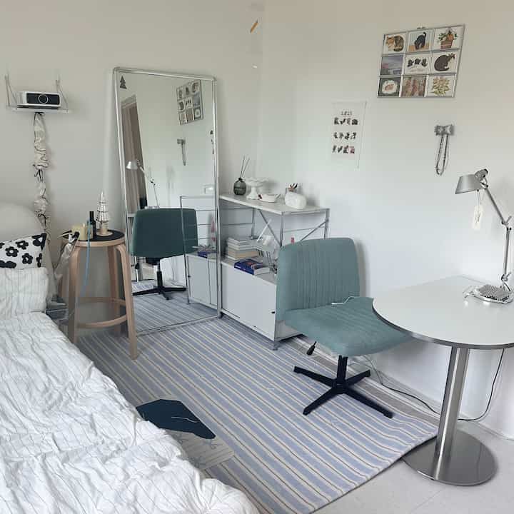 Bright small bedroom with white and blue tones featuring mid-century modern furniture, desk, and rug creating a clean atmosphere