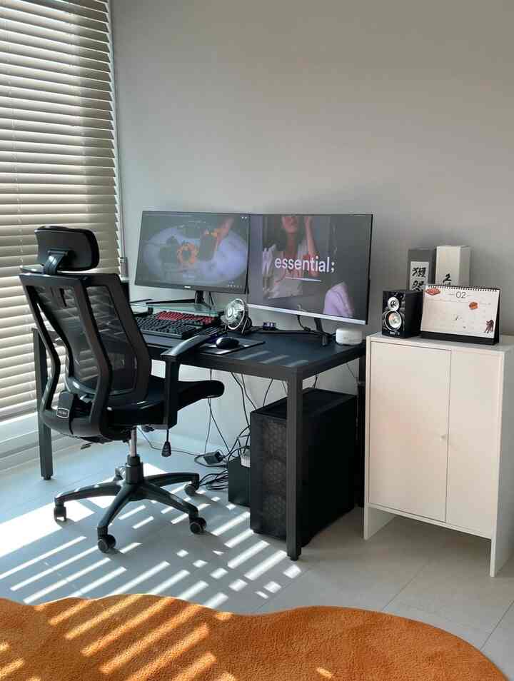 ブラックトーンのホームオフィス、ブラックデスクとデュアルモニター、ブラックメッシュチェアが配置された集中感のある空間