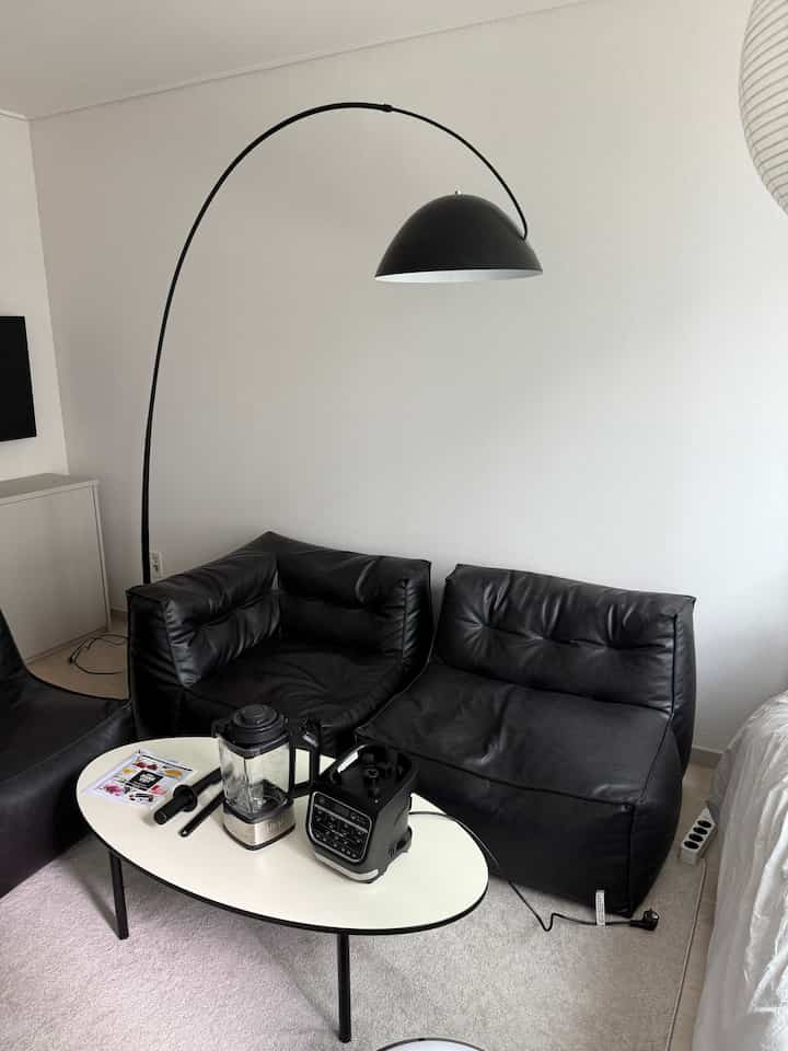 白い壁とラグのあるモダンなリビングルーム、黒のビーンバッグソファとフロアランプ、白いコーヒーテーブルが配置された落ち着いた空間