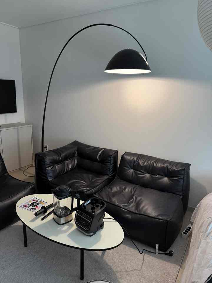白い壁と黒いビーズクッションソファ、アーク型フロアランプが配置されたモダンなリビングルーム