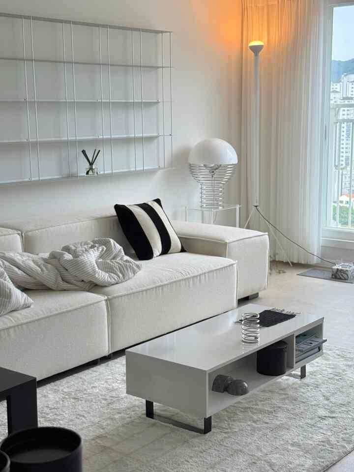 A white and monotone living room featuring a cream sofa, simple table, and sleek lighting with a modern clean atmosphere