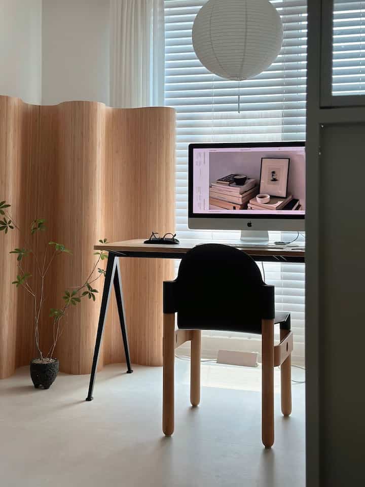 Monotone and wood tone study featuring a clean desk and chair, wood room divider, and a small plant in a calm home office space