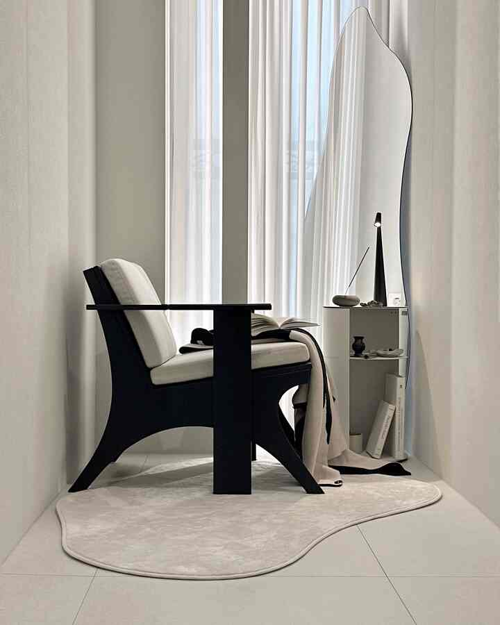 Monotone white and black small corner space featuring black armchair, white rug, large irregular mirror with natural modern style