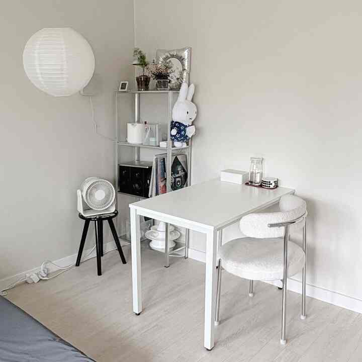 白を基調とした寝室に配置されたダイニング兼デスクとクッションチェアがあるミニマルで清潔感のあるインテリア