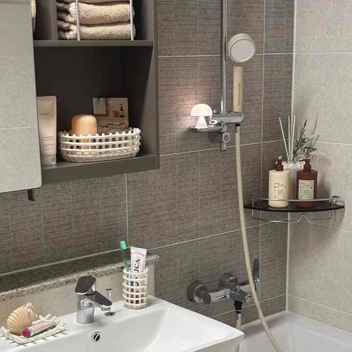 ベージュとグレーの色調のバスルーム、洗面台とシャワー、タオルやディフューザーが整然と配置された印象的な空間