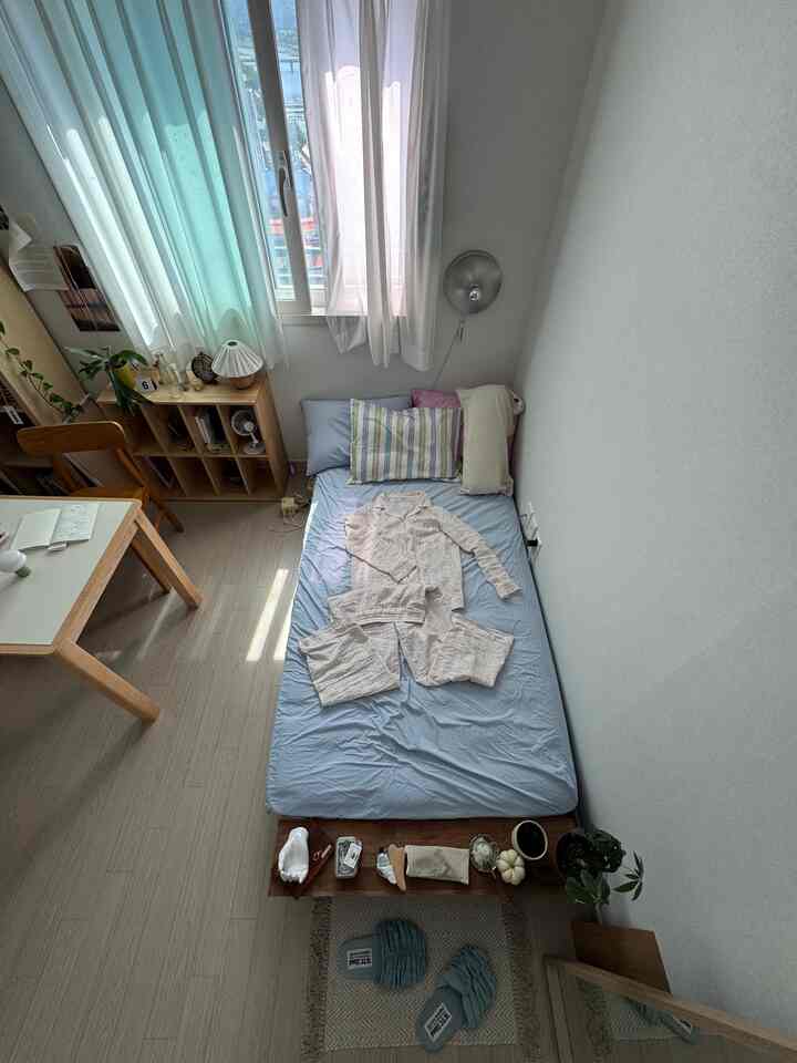 明るい木目調とホワイト、ブルーのカーテンがある一人用寝室、自然光とミッドセンチュリーモダンの家具が配置された落ち着いた空間