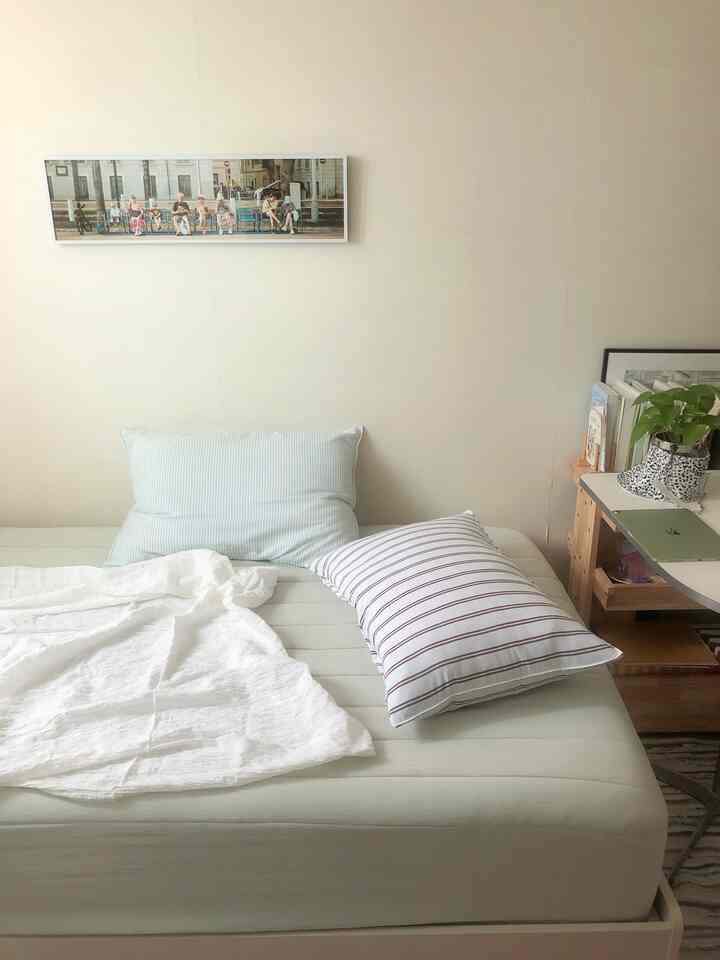 白とベージュのトーンの一人暮らしの寝室、マットレスとクッションが配置された落ち着いた空間