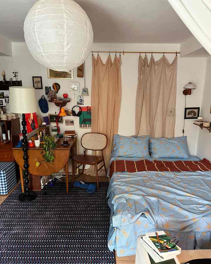 ナチュラルカラーとベージュのカーテン、青い寝具が印象的な、居心地の良い寝室と小さな机のある空間