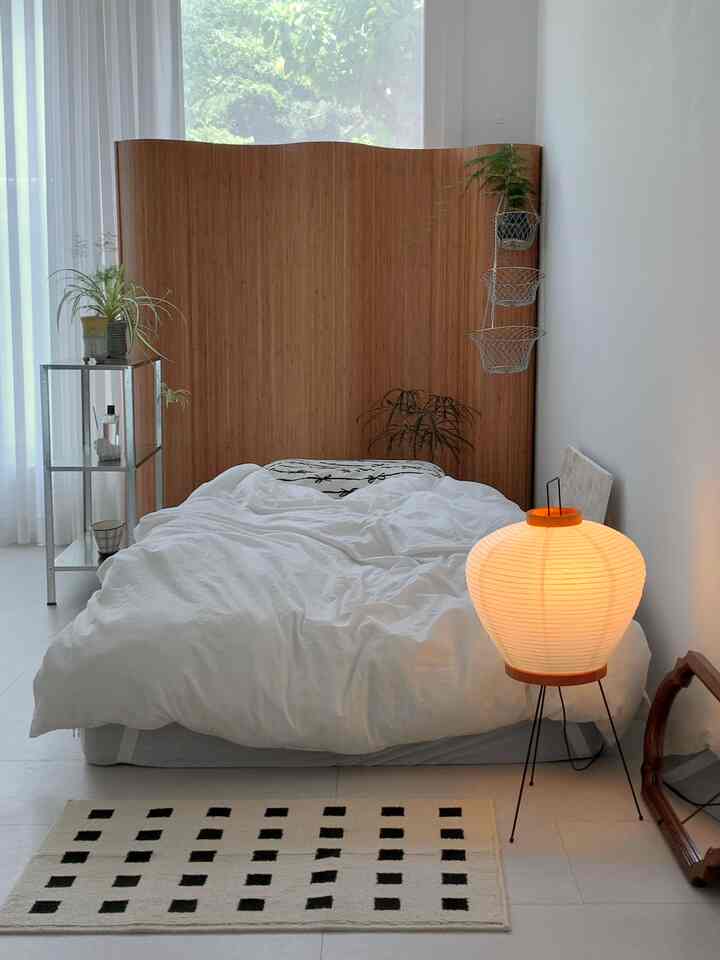 Cozy bedroom featuring white and wood tones with a large wooden room divider and paper floor lamp in a simple layout