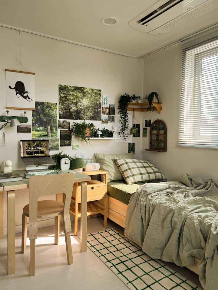 ナチュラルな木目調と穏やかな緑色が調和したワンルーム寝室、ベッドとデスク、植物が配された雰囲気のあるインテリア