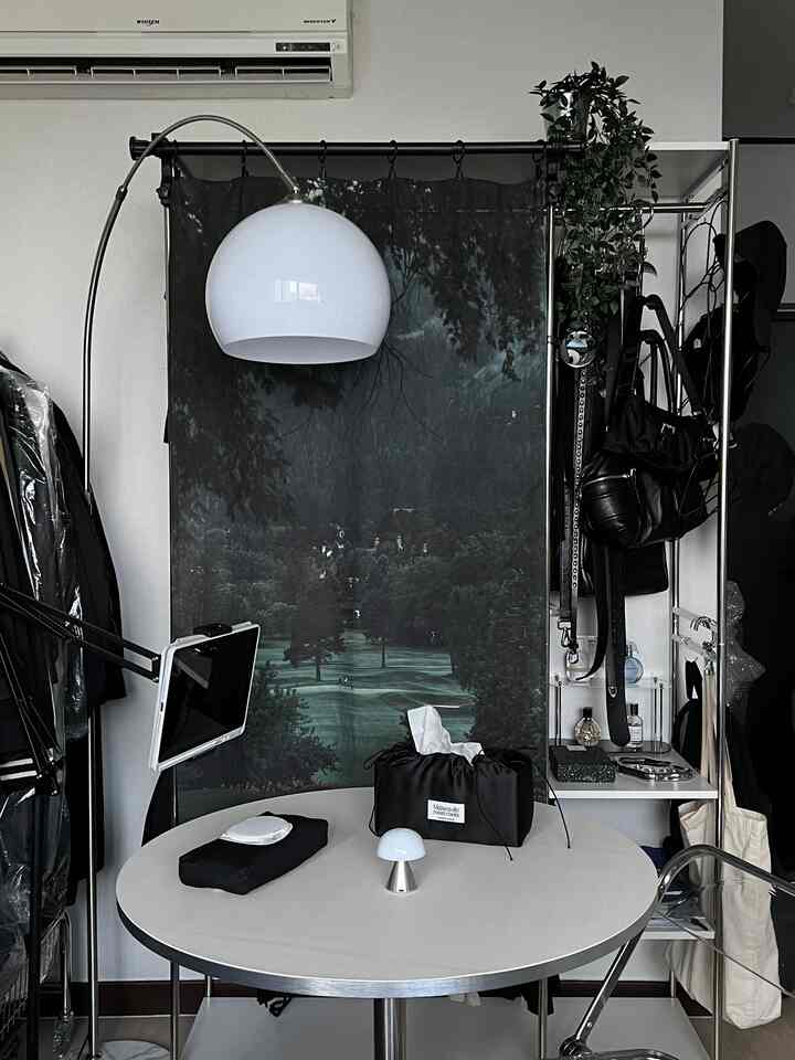 ホワイトとブラックのトーンのコンパクトな部屋、丸テーブルとフロアランプ、カーテンと収納スペースが配置されたインテリア