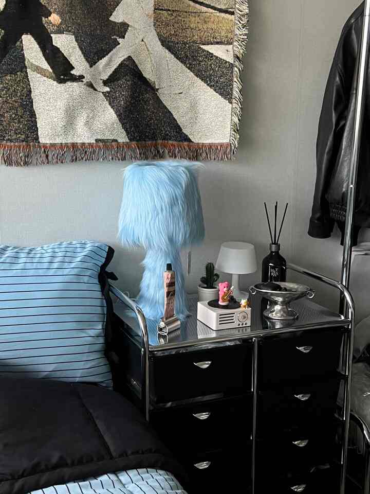 青と黒の色調の寝室、ミッドセンチュリーモダンスタイルのクローム製サイドテーブルとふわふわの青いフロアランプが配置された落ち着いた空間