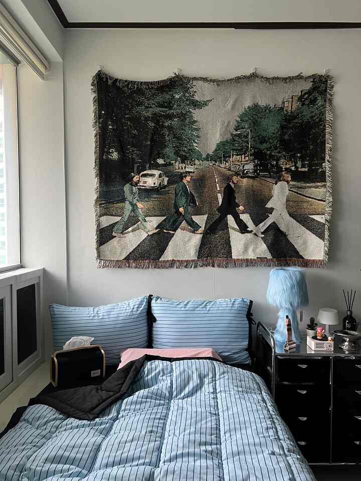 ブルーの色調のワンルーム寝室、有名なビートルズのタペストリーポスターと居心地の良い寝具が配置された個人的な空間