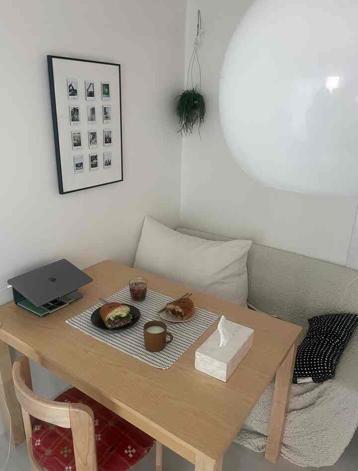 白い壁とナチュラルな木製テーブルがある居心地の良いリビング、おうちカフェ空間としてソファとコーヒー、簡単な昼食が配置されたミニマルなインテリア