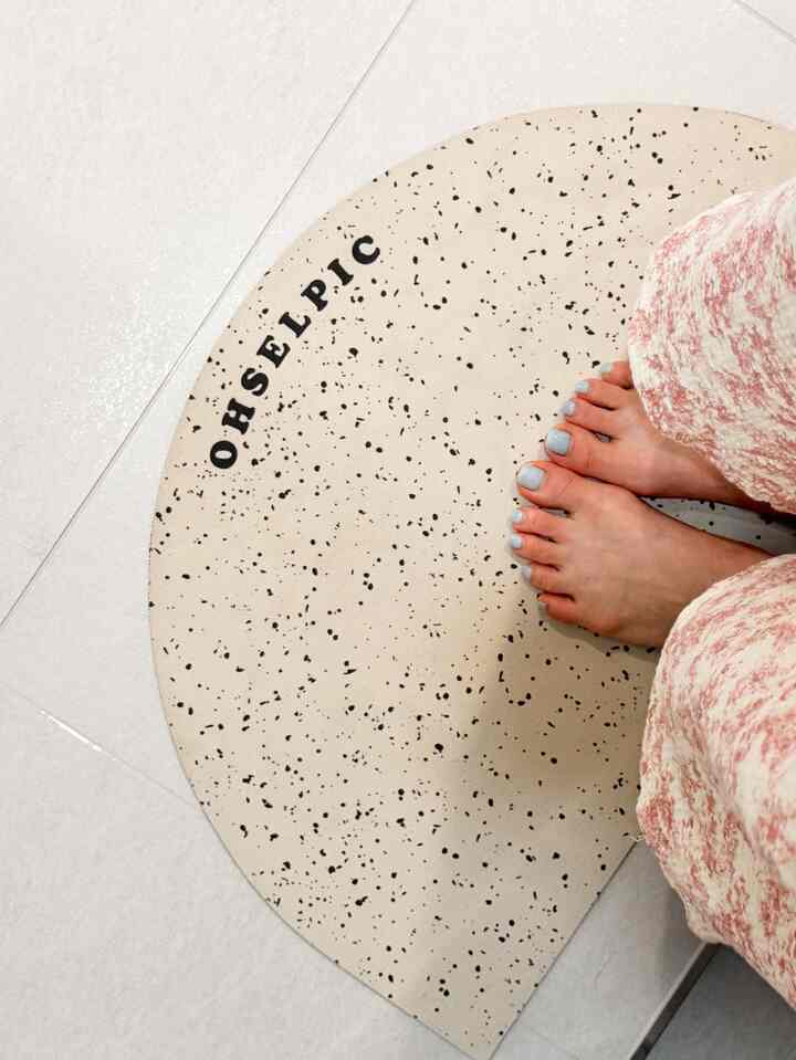 ベージュの半円形の珪藻土バスマットと白いタイルの床に足をのせている様子