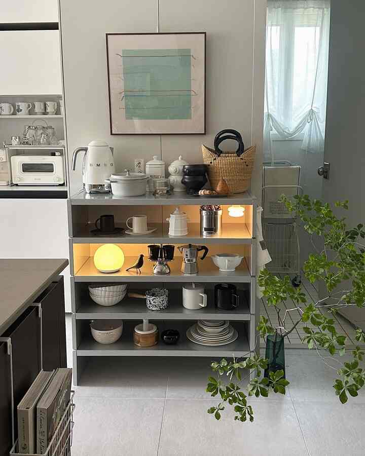 白とグレーのトーンのキッチン、スチール棚にコーヒー用品やオブジェ、多様なグリーンプラントが配置された雰囲気あるインテリア