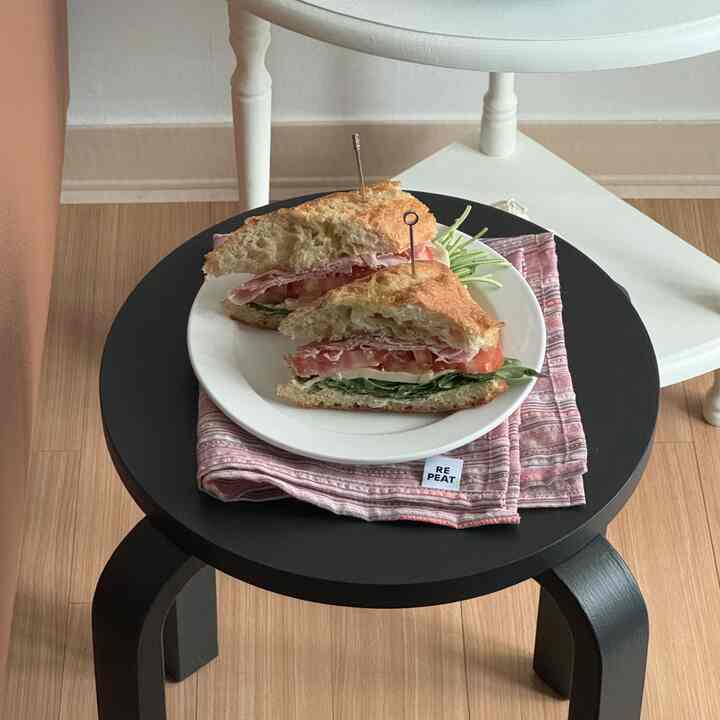 ウッドトーンの空間にキッチンの雰囲気があり、黒いスツールの上に皿とピンクのストライプのランチョンマットが配置されたインテリア