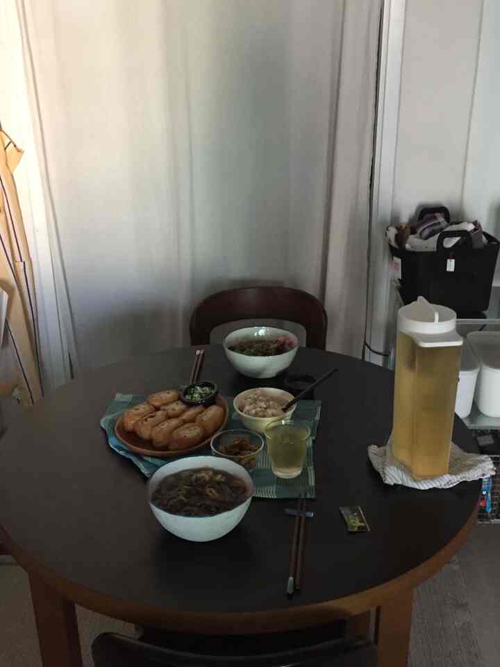 ナチュラルな色調のダイニングルーム、丸い木製テーブルに様々な食器と飲み物が配置された雰囲気のあるインテリア