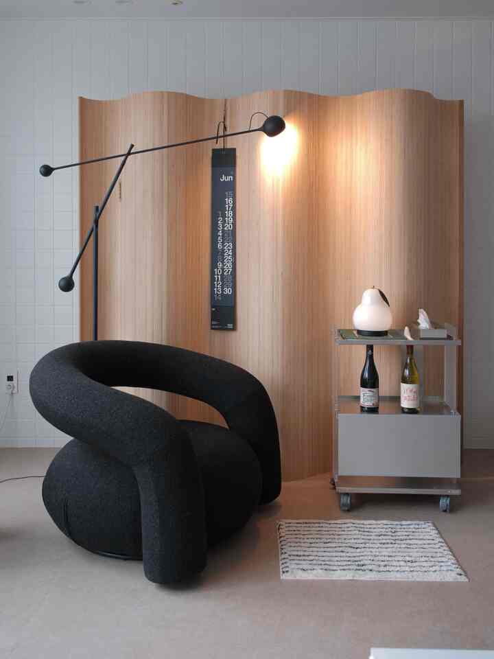 Modern living room with natural wood-toned divider, black armchair, and metal bar cart