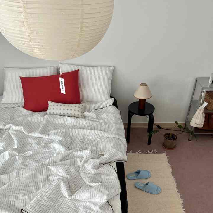 ホワイトトーンの寝室、白い寝具と赤いアクセントピロー、ブルーのスリッパが配置された清潔でモダンなナチュラルインテリア