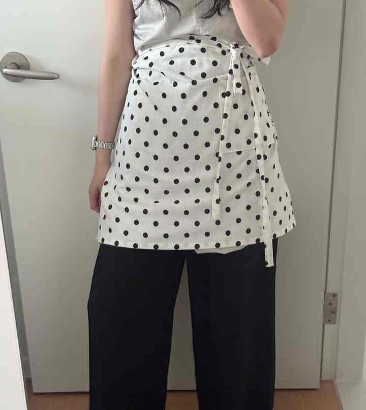 白地に黒のドット柄エプロンを着用した人物、シンプルな背景の室内空間