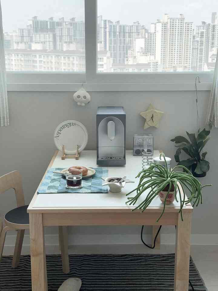 ライトブラウンと白を基調としたコンパクトなキッチンスペース、ダイニングテーブルにはコーヒーマシンと食器が配置され、ナチュラルな雰囲気のホームカフェインテリア