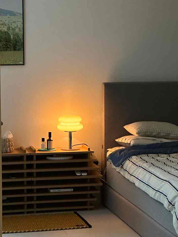 グレーのベッドと木製のナイトテーブルが配置された、落ち着いた雰囲気のシンプルでナチュラルな寝室