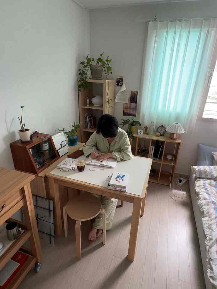 白い壁とナチュラルトーンの家具が配置された6畳の寝室、デスクとスツールが中心で明るいカーテンが窓を飾る雰囲気のあるインテリア