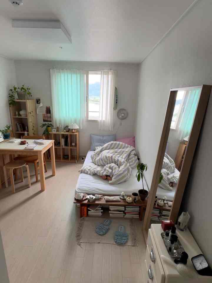 明るいアイボリーと木目調の一人暮らし用寝室、デスクと本棚が配置された落ち着いた空間