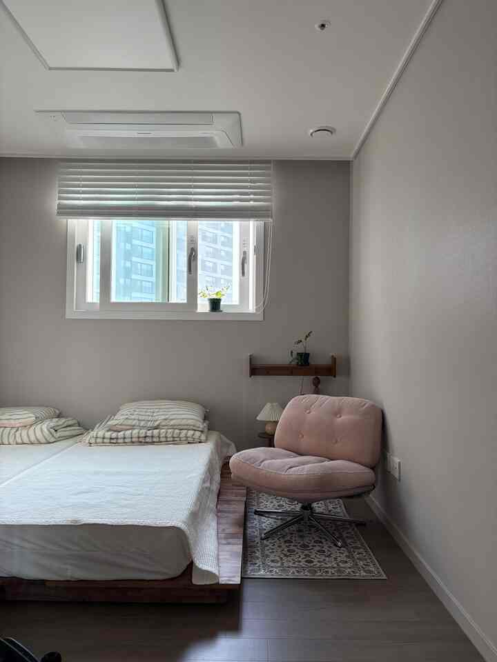 白とナチュラルな色調の子供部屋、柔らかいピンクのアームチェアと低床ベッドが配置された雰囲気のあるインテリア