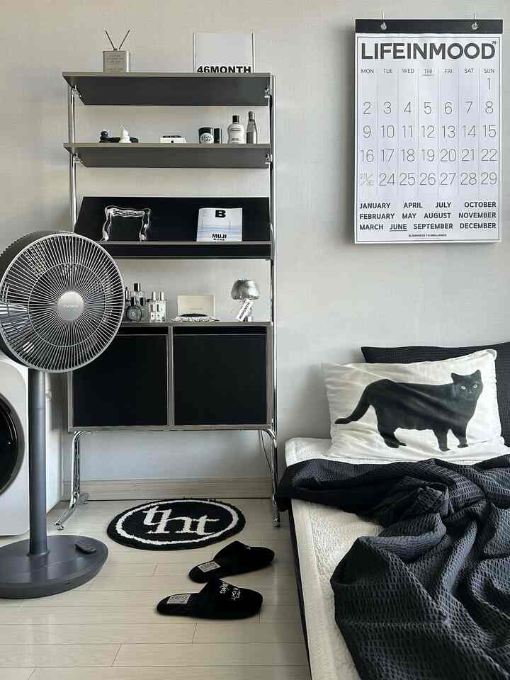 黒と白のトーンの寝室、ミッドセンチュリーモダンスタイルのキャビネットと棚、扇風機、猫柄のクッションが配置された印象的なインテリア
