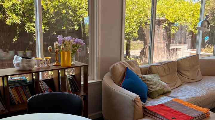 Bright natural light fills a natural modern living room featuring a beige leather sofa and a wooden shelf with a yellow vase