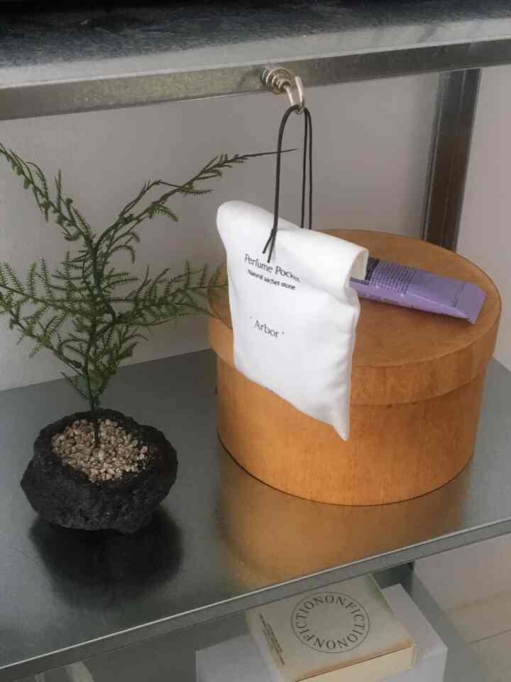 ナチュラルウッドの丸箱と金属製の棚に造花とディフューザーポケットが置かれたシンプルなワンルームの棚のインテリア