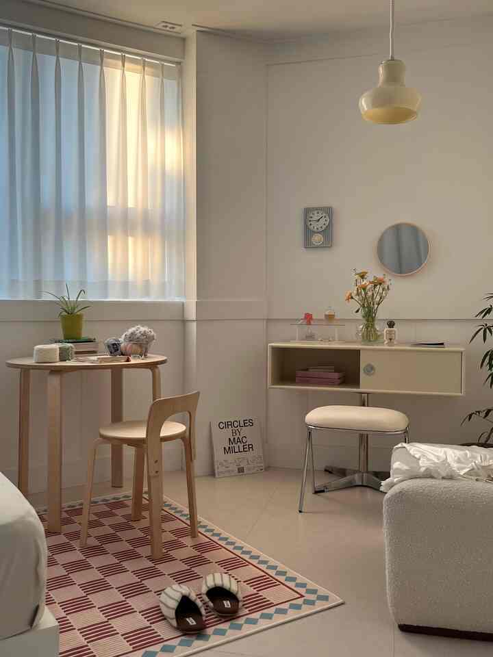 Soft natural-toned small living room space featuring a wooden table and chair, cream stool, and patterned rug creating a cozy interior