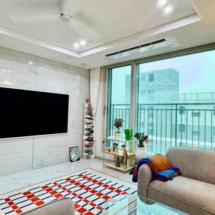 白い大理石の壁と床、大きな窓とグレーのソファが配置された明るく清潔なリビング