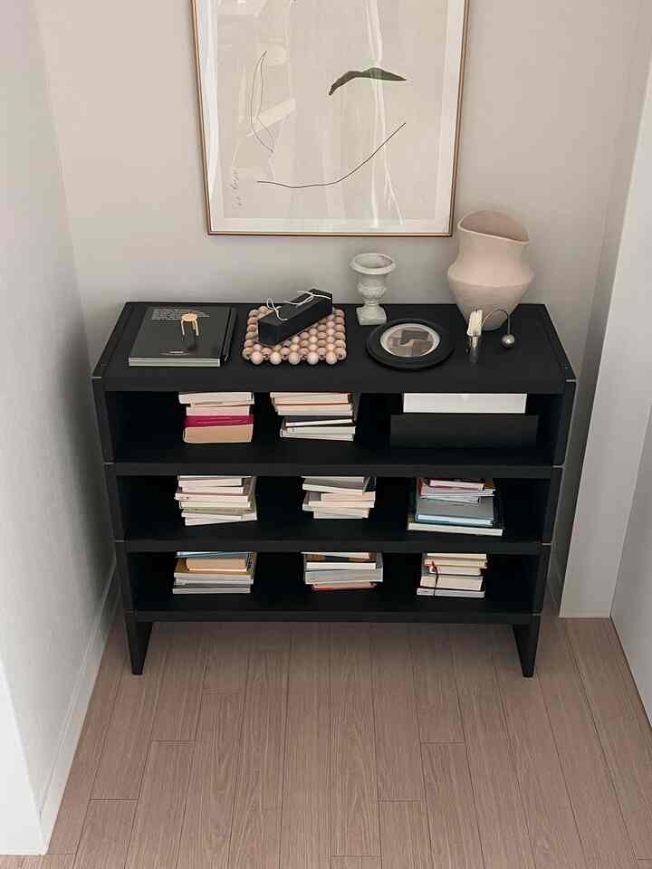 ナチュラルカラーの狭い書斎に黒い棚と多くの本、抽象的なウォールアートが配置されたミニマルなインテリア