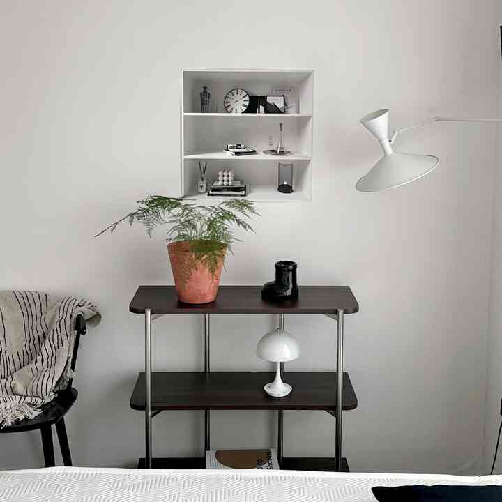 A white and brown toned bedroom featuring a mid-century modern shelf with plants and lighting in a simple and natural setting