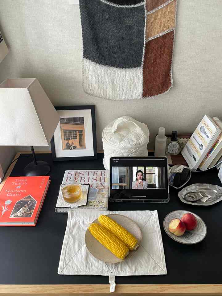 Black tabletop with tablecloth, corn, and fruit, featuring a tablet, books, and lamp arranged, a natural-toned home cafe space