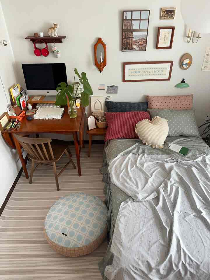 ナチュラルな木目調とグリーンの寝具が調和した6畳の寝室、デスクと多様なクッションが心地よい空間を作り出す