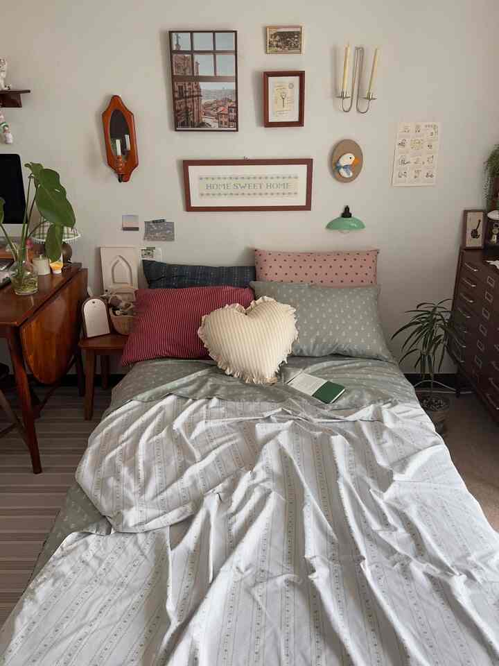 ナチュラルな色調の寝室、様々な色の枕とクッションが配置されたベッドと壁に掛けられた額縁が印象的な落ち着いた空間