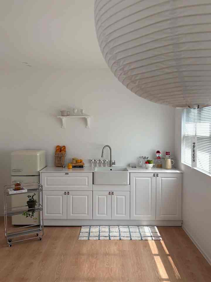 A white and wood tone kitchen space featuring a clean sink, window blinds, and a patterned rug creating a warm atmosphere