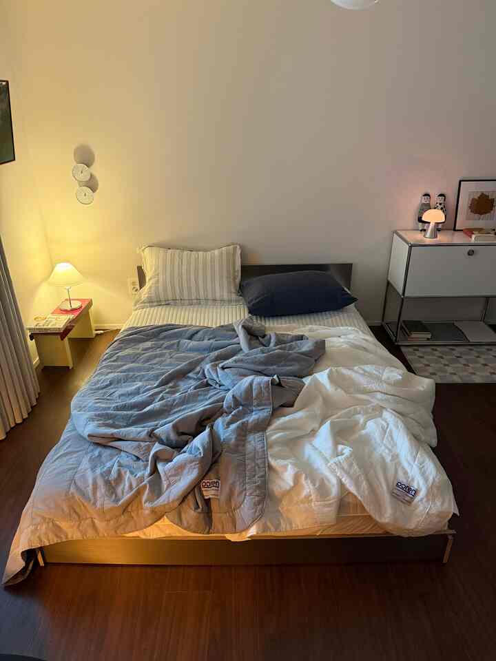 Modern bedroom with white walls and wood tone flooring featuring a bed dressed in blue and white summer bedding alongside a mid-century modern storage cabinet