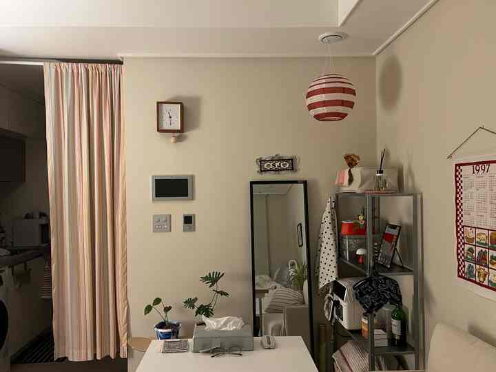 ベージュトーンのリビング、壁掛け時計と大きな全身鏡が配置され、植物のあるナチュラルで落ち着いた雰囲気のインテリア