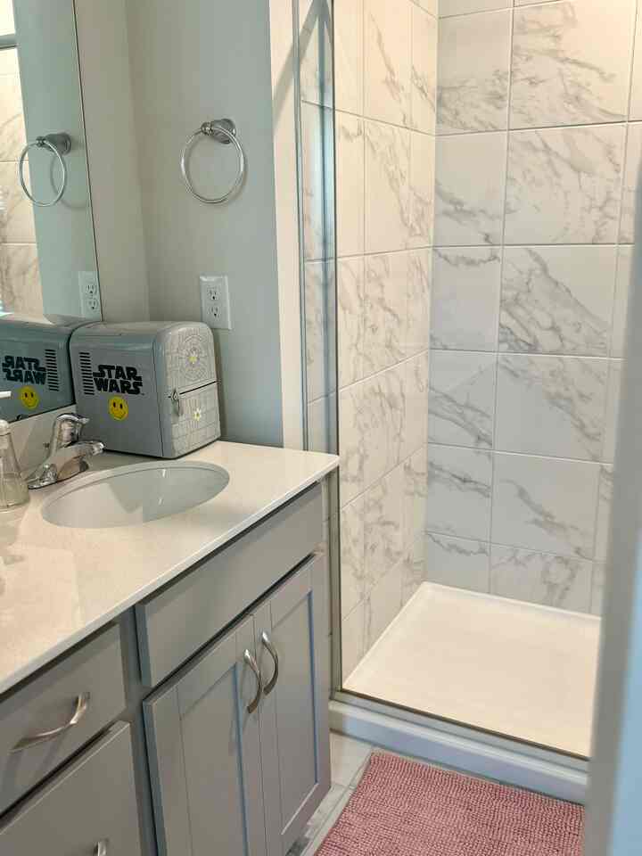 Modern white and gray bathroom featuring marble tile shower area and a pink bath mat with a clean aesthetic