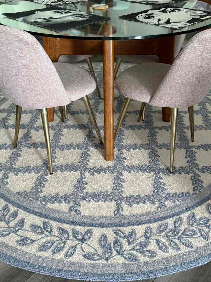 Round dining table with wood legs and pink dining chairs on a blue-patterned rug, creating a French country style dining room ambiance