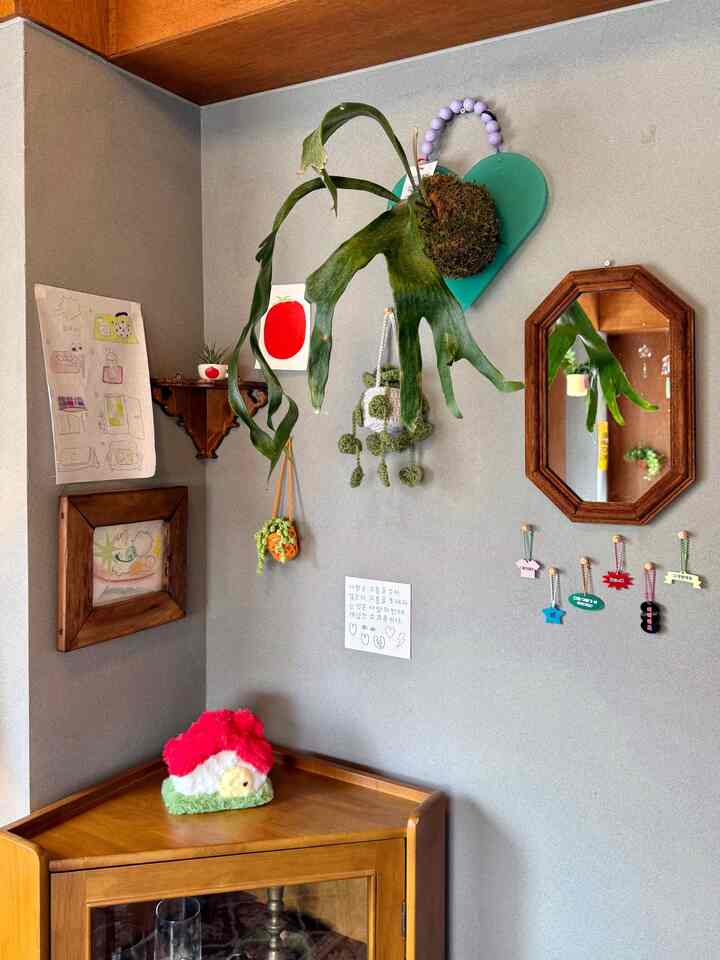 ナチュラルな色調のコーナースペース、木製家具と観葉植物、壁の装飾が配された温かみのあるインテリア